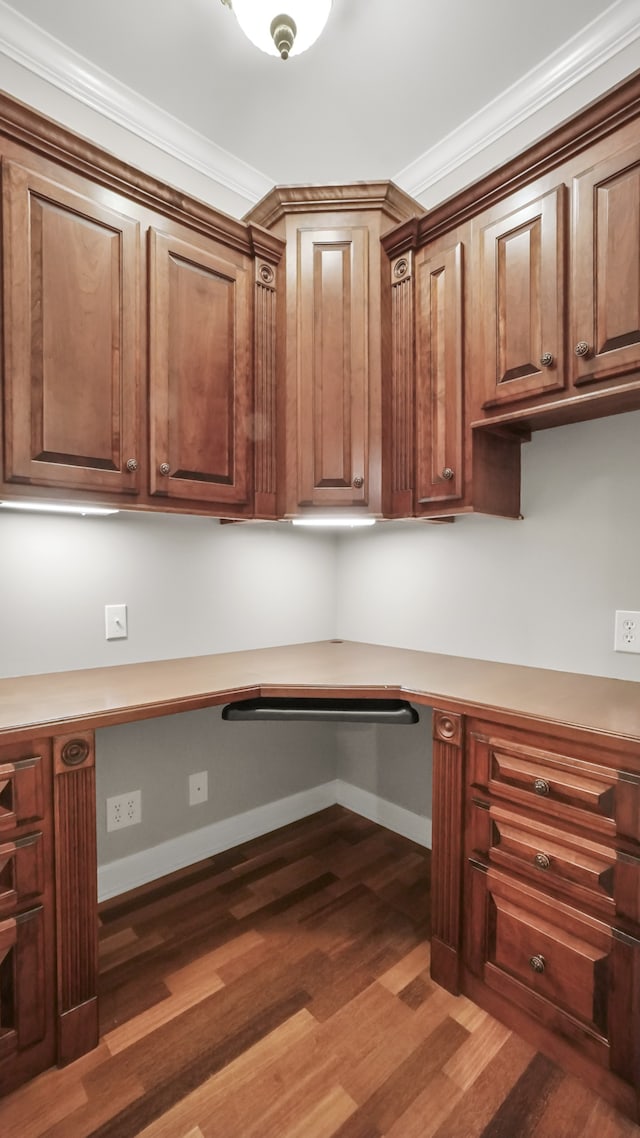 unfurnished office featuring built in desk, dark wood-type flooring, and ornamental molding