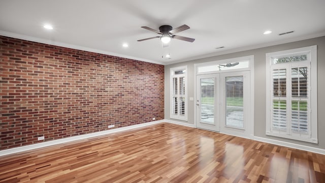 empty room with hardwood / wood-style floors, ceiling fan, crown molding, and brick wall