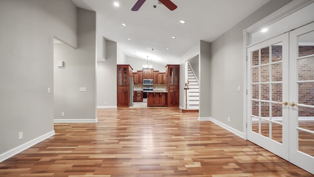 unfurnished living room featuring ceiling fan with notable chandelier, high vaulted ceiling, and light hardwood / wood-style flooring