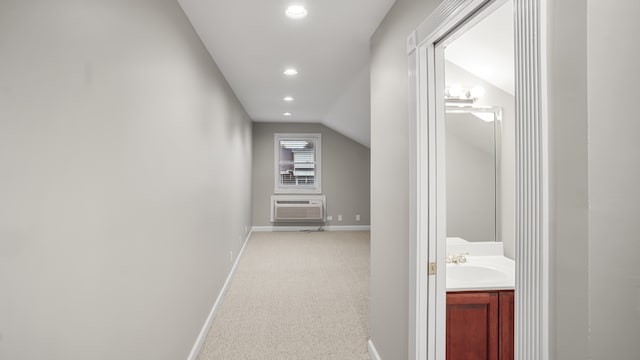 corridor with light carpet, a wall mounted AC, lofted ceiling, and sink