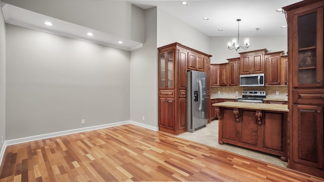 kitchen with high vaulted ceiling, decorative light fixtures, appliances with stainless steel finishes, a notable chandelier, and light hardwood / wood-style floors