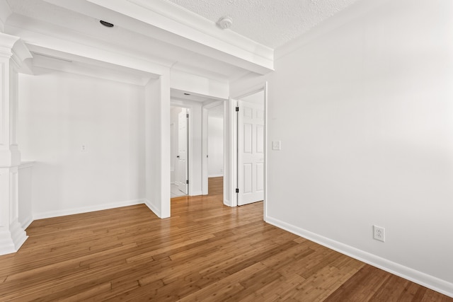 unfurnished room featuring wood-type flooring, a textured ceiling, ornate columns, and ornamental molding