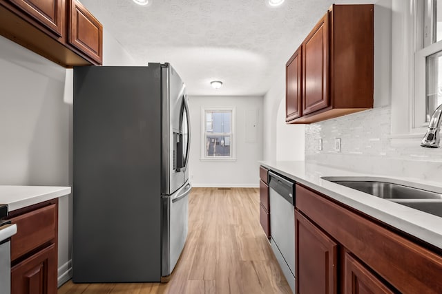 kitchen with sink, appliances with stainless steel finishes, a textured ceiling, backsplash, and light wood-type flooring