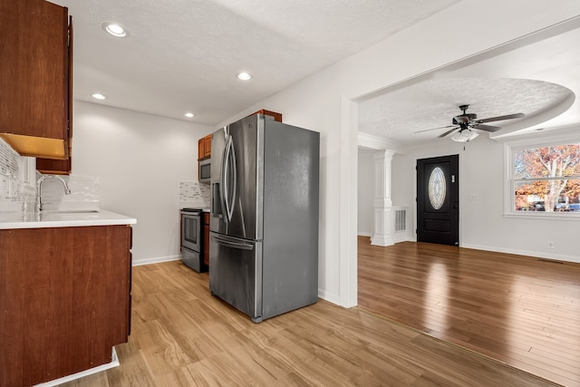 kitchen featuring ornate columns, light wood-type flooring, stainless steel appliances, and a textured ceiling