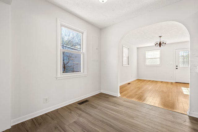 spare room with a textured ceiling, light hardwood / wood-style flooring, plenty of natural light, and a notable chandelier