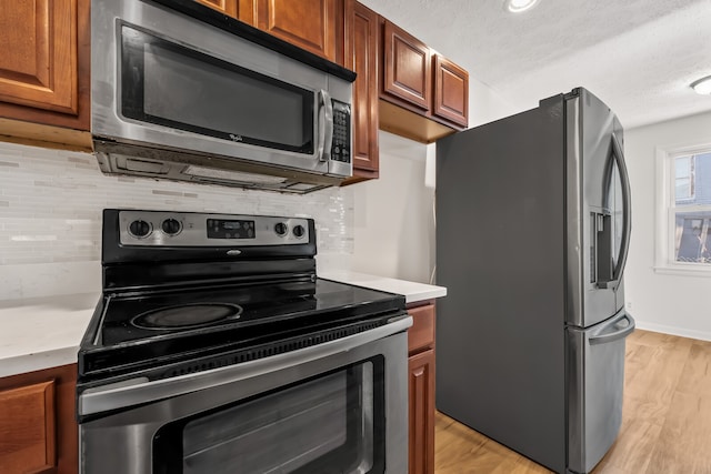 kitchen featuring a textured ceiling, light wood-type flooring, stainless steel appliances, and tasteful backsplash