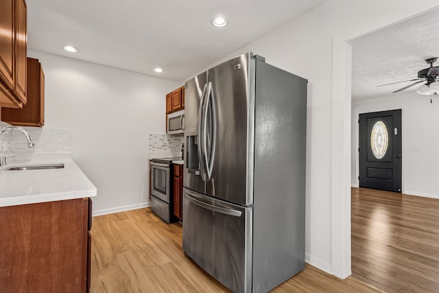 kitchen with sink, tasteful backsplash, a textured ceiling, appliances with stainless steel finishes, and light wood-type flooring