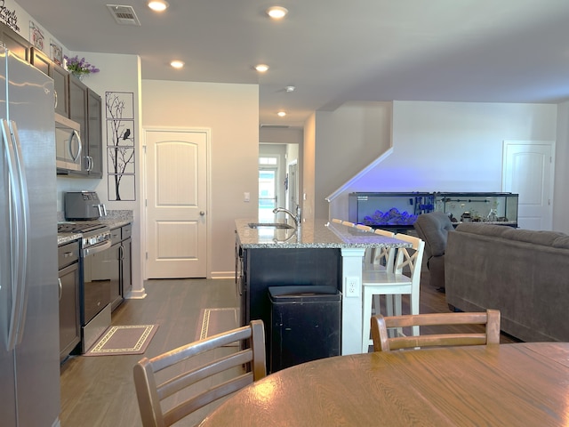 kitchen featuring sink, a center island with sink, dark hardwood / wood-style flooring, stainless steel appliances, and light stone counters