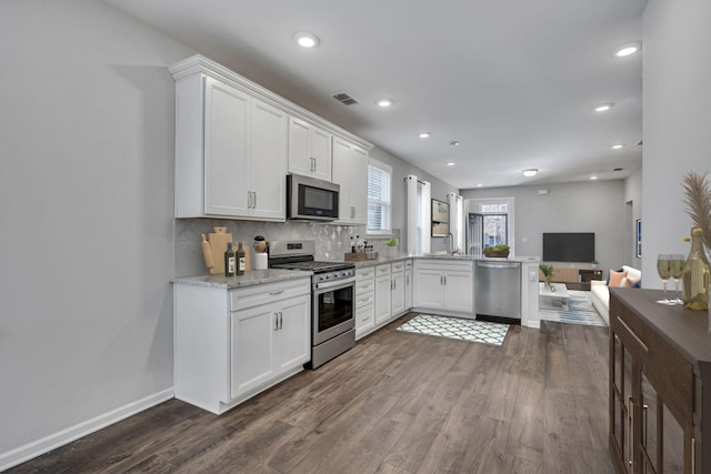 kitchen with appliances with stainless steel finishes, white cabinetry, kitchen peninsula, dark wood-type flooring, and backsplash