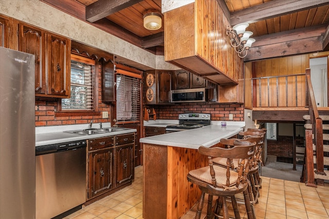 kitchen featuring a breakfast bar, beamed ceiling, light tile patterned floors, wood ceiling, and stainless steel appliances