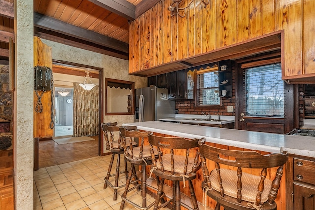 kitchen with sink, light tile patterned flooring, pendant lighting, beam ceiling, and stainless steel fridge