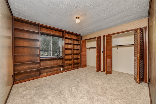 unfurnished bedroom featuring a textured ceiling, light colored carpet, and multiple closets