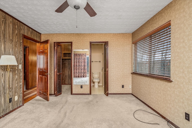 unfurnished bedroom featuring a textured ceiling, light colored carpet, ensuite bath, and ceiling fan