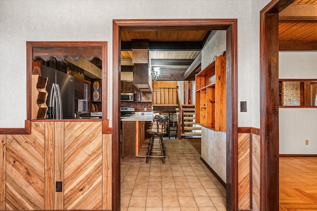 kitchen featuring a kitchen bar, appliances with stainless steel finishes, light tile patterned floors, wooden ceiling, and beamed ceiling