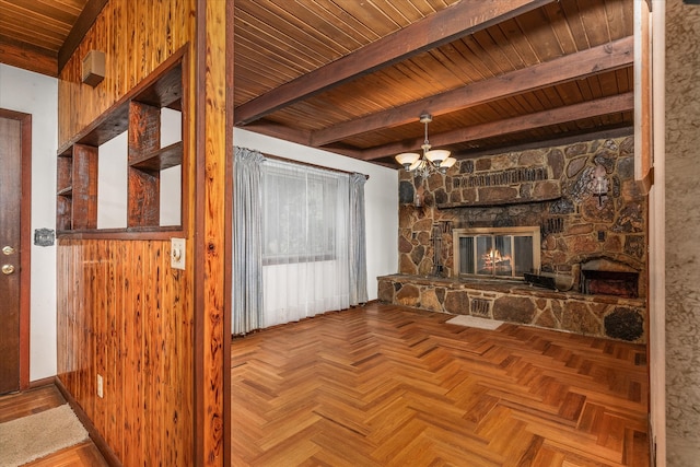 unfurnished living room with beam ceiling, a stone fireplace, wooden walls, and wooden ceiling