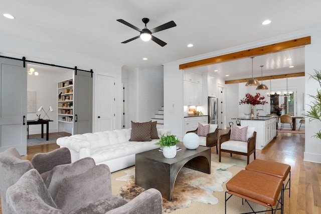 living room with a barn door, light hardwood / wood-style floors, ceiling fan, and ornamental molding