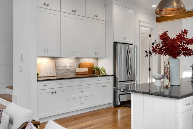 kitchen with backsplash, stainless steel fridge, dark stone counters, white cabinets, and light wood-type flooring