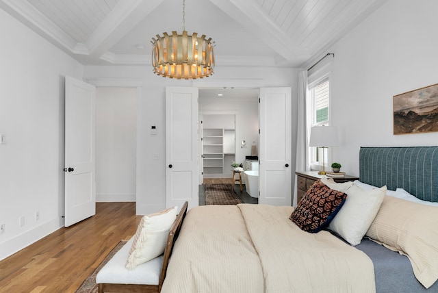 bedroom with beam ceiling, a walk in closet, hardwood / wood-style flooring, and an inviting chandelier