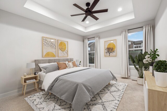 bedroom with light carpet, a raised ceiling, and ceiling fan