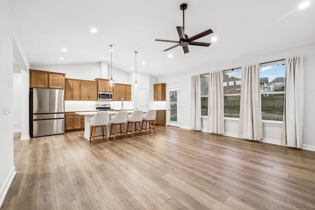 kitchen featuring a kitchen bar, hanging light fixtures, a kitchen island with sink, stainless steel appliances, and light hardwood / wood-style floors