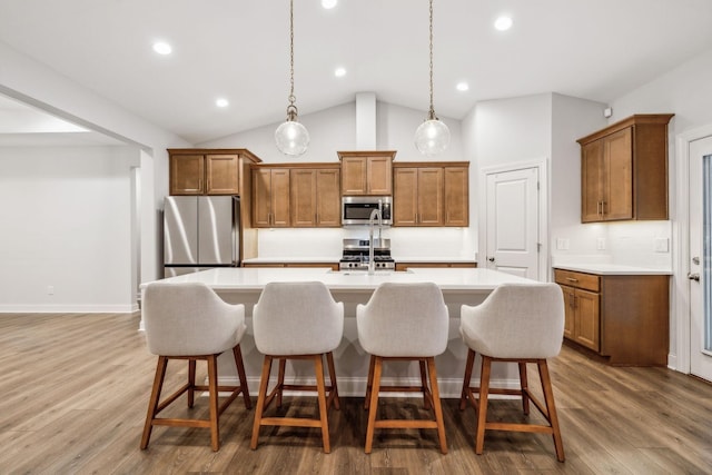 kitchen with hanging light fixtures, a kitchen breakfast bar, stainless steel appliances, wood-type flooring, and an island with sink