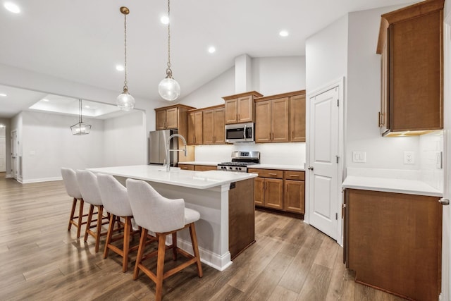 kitchen with dark wood-type flooring, appliances with stainless steel finishes, a kitchen island with sink, hanging light fixtures, and a kitchen breakfast bar