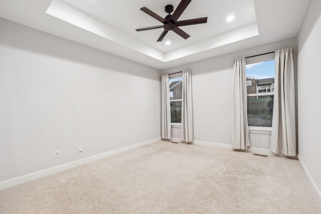 carpeted empty room with a raised ceiling and ceiling fan