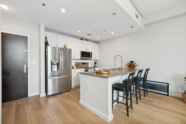 kitchen featuring light hardwood / wood-style flooring, white cabinetry, sink, dark stone countertops, and appliances with stainless steel finishes