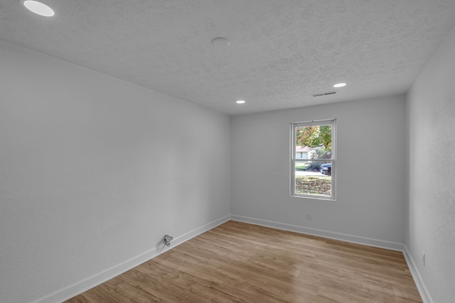 spare room with a textured ceiling and light wood-type flooring