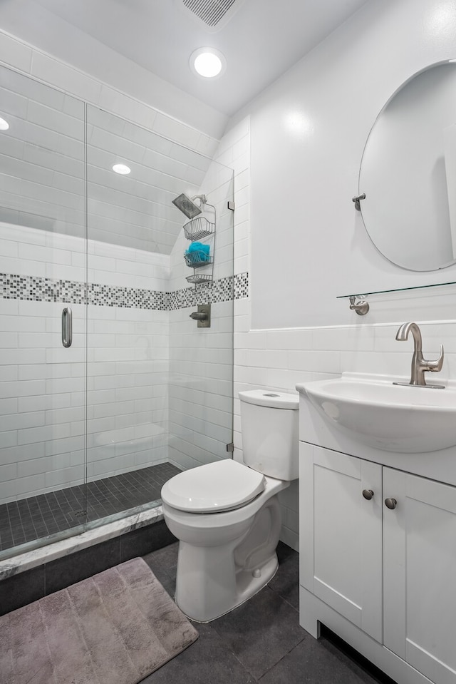 bathroom with vanity, toilet, tile walls, tile patterned flooring, and a shower with shower door