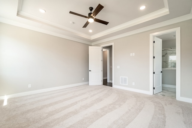 unfurnished bedroom featuring ensuite bath, ceiling fan, a raised ceiling, and light carpet