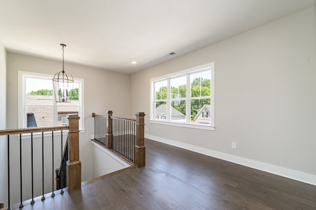 unfurnished room featuring a wealth of natural light, dark hardwood / wood-style flooring, and an inviting chandelier