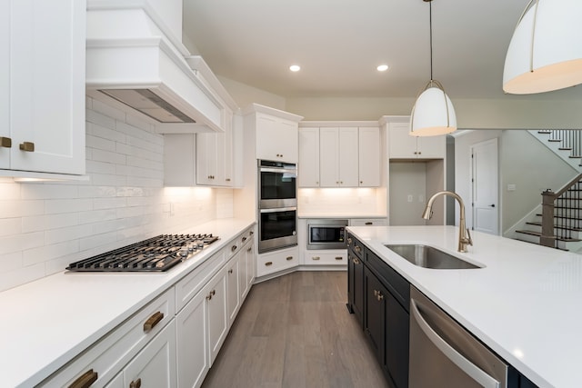 kitchen with white cabinetry, sink, hardwood / wood-style floors, hanging light fixtures, and stainless steel appliances