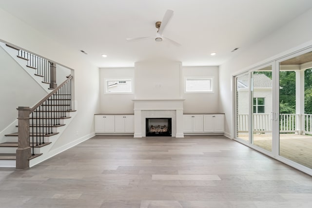 unfurnished living room featuring ceiling fan, a tile fireplace, and light wood-type flooring