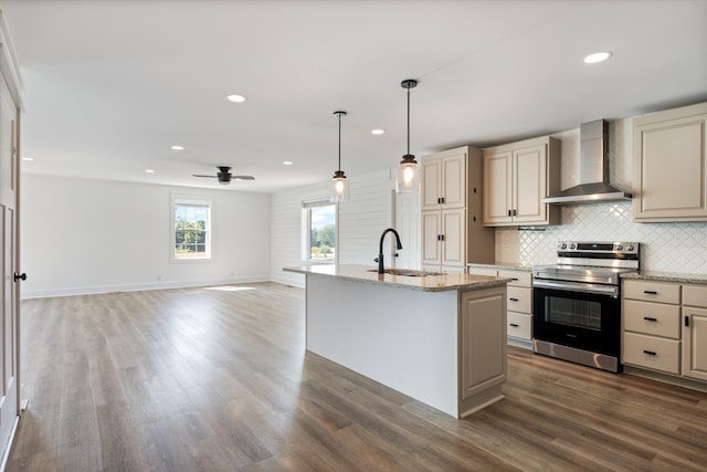 kitchen featuring dark wood-type flooring, a center island with sink, stainless steel range with electric stovetop, and wall chimney range hood