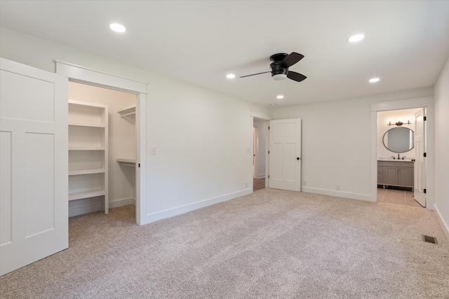 unfurnished bedroom with a spacious closet, connected bathroom, ceiling fan, and light colored carpet