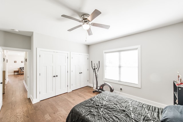 bedroom with light hardwood / wood-style floors, ceiling fan, and multiple closets