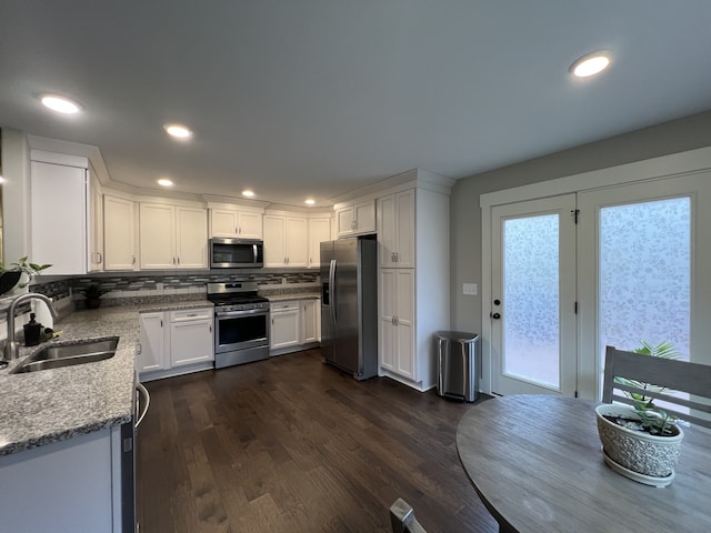 kitchen with light stone counters, stainless steel appliances, sink, white cabinets, and dark hardwood / wood-style floors