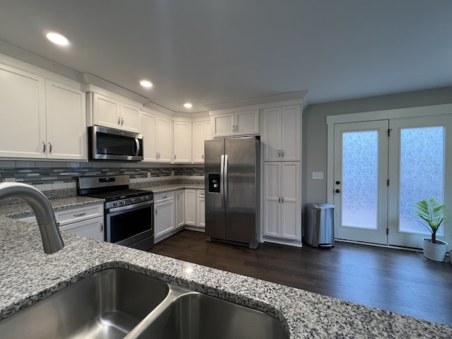 kitchen with white cabinets, appliances with stainless steel finishes, dark hardwood / wood-style flooring, and light stone counters