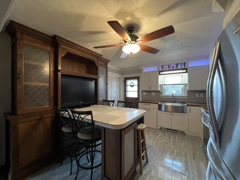 kitchen featuring a kitchen breakfast bar, white cabinetry, sink, stainless steel refrigerator, and backsplash