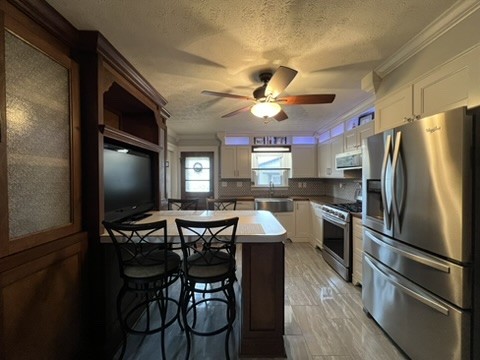 kitchen featuring appliances with stainless steel finishes, backsplash, a breakfast bar, ceiling fan, and white cabinets