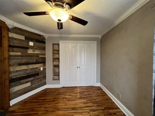 unfurnished bedroom featuring ceiling fan, dark hardwood / wood-style floors, crown molding, a textured ceiling, and wooden walls