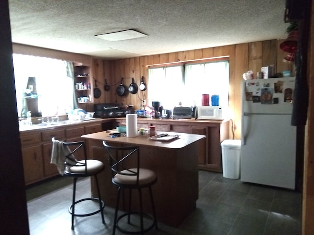 kitchen featuring a center island, white appliances, a textured ceiling, and wooden walls