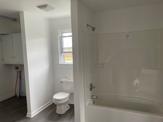 bathroom with shower / bath combination, wood-type flooring, and toilet