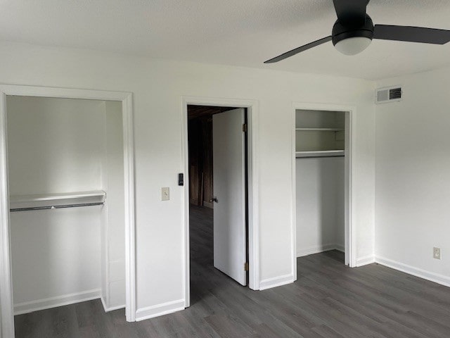 unfurnished bedroom featuring ceiling fan, dark hardwood / wood-style floors, and multiple closets