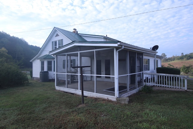 view of property exterior with central air condition unit, a sunroom, and a lawn