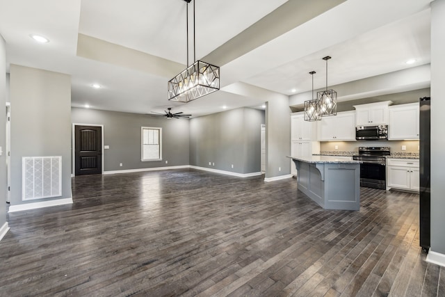 kitchen with white cabinets, a kitchen island, appliances with stainless steel finishes, dark wood-type flooring, and decorative light fixtures