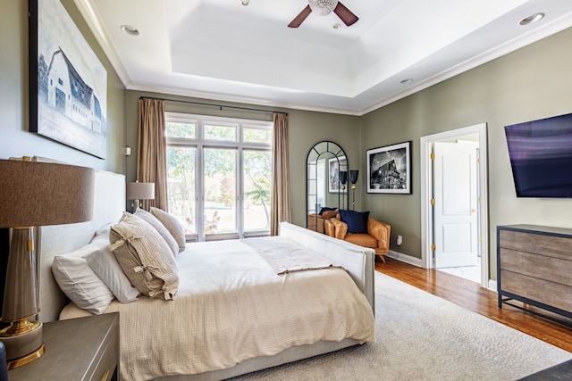 bedroom featuring baseboards, a raised ceiling, a ceiling fan, ornamental molding, and wood finished floors