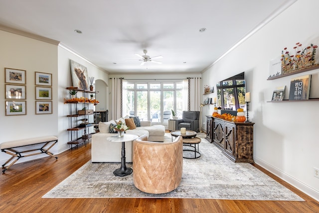 living area with crown molding, baseboards, arched walkways, and wood finished floors