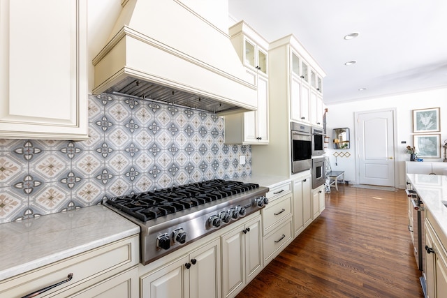 kitchen featuring appliances with stainless steel finishes, backsplash, dark wood finished floors, glass insert cabinets, and custom range hood